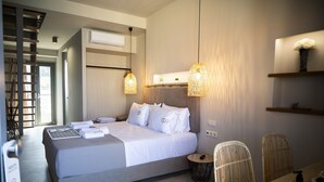 Una habitación de hotel moderna con una cama grande, una mesa de comedor, sillas de mimbre y una mesita auxiliar.
