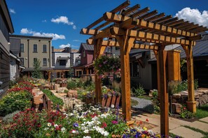 A garden with a wooden pergola, various flowers, and a stone pathway.