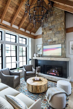 A spacious living room with a stone fireplace, large windows, and a chandelier. - The Mariposa-Valerian Bundle at Academy Place (Crested Butte)