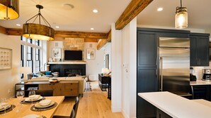 Une cuisine moderne dotée d’un grand réfrigérateur en acier inoxydable, de poutres en bois au plafond et d’un coin repas avec une longue table dressée pour quatre personnes.