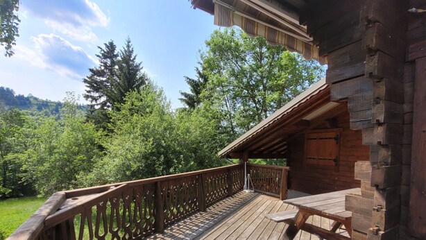 Um deck de madeira com guarda-corpo, um banco e vista para uma área arborizada.