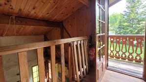 Uma cabana de madeira com varanda, um extintor de incêndio e vista para o verde lá fora.