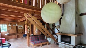 Ampla sala de estar com escada de madeira, lareira e sofá.