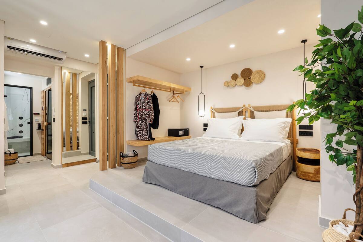 A modern bedroom with a bed, bedside tables, a hanging coat rack, and a large green plant.
