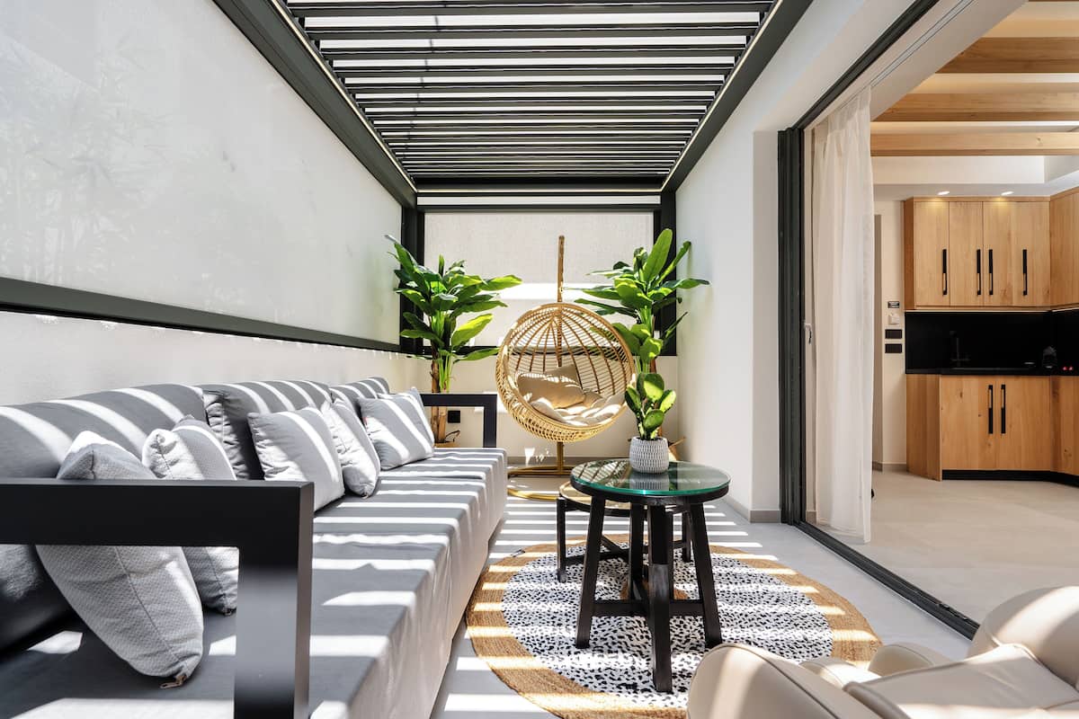 A modern living room with a sofa, a round table, and a hanging chair. There is a kitchen visible through an open door.