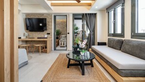 A modern living room with a sofa, a coffee table, a TV, and a dining area. - Legato Spa Suites (Naxos)