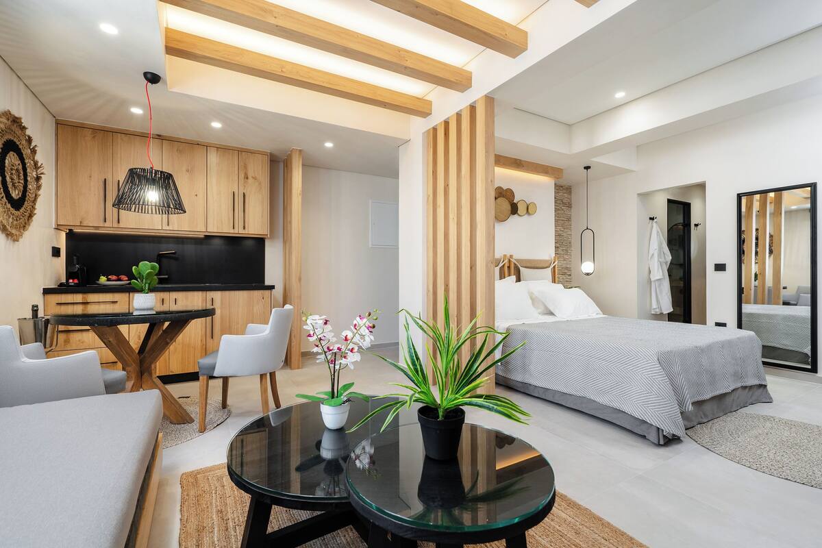 A modern hotel room with a bed, a dining area, and a kitchen.