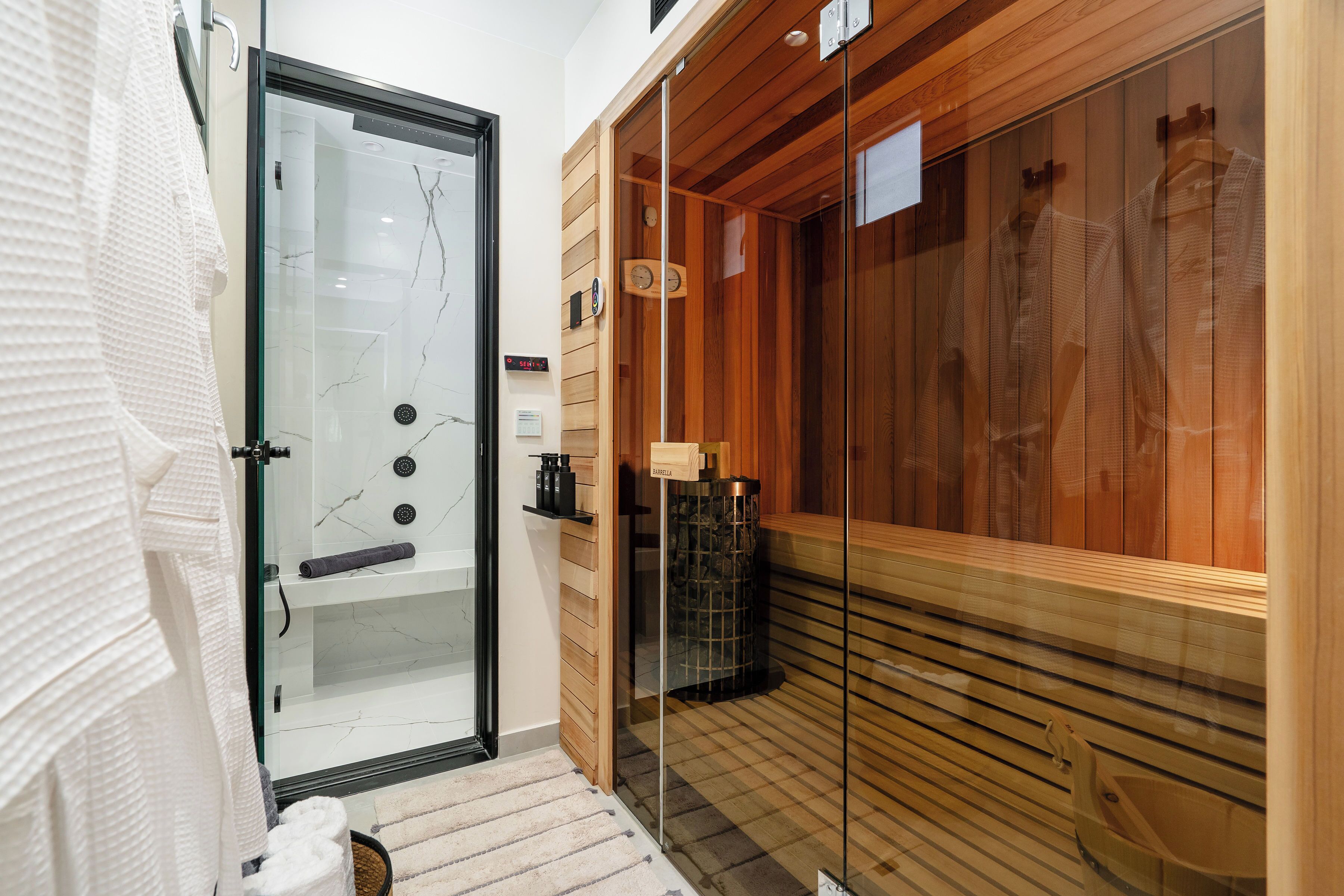 Een moderne badkamer met een glazen douchecabine, een houten sauna en een handdoekrek.