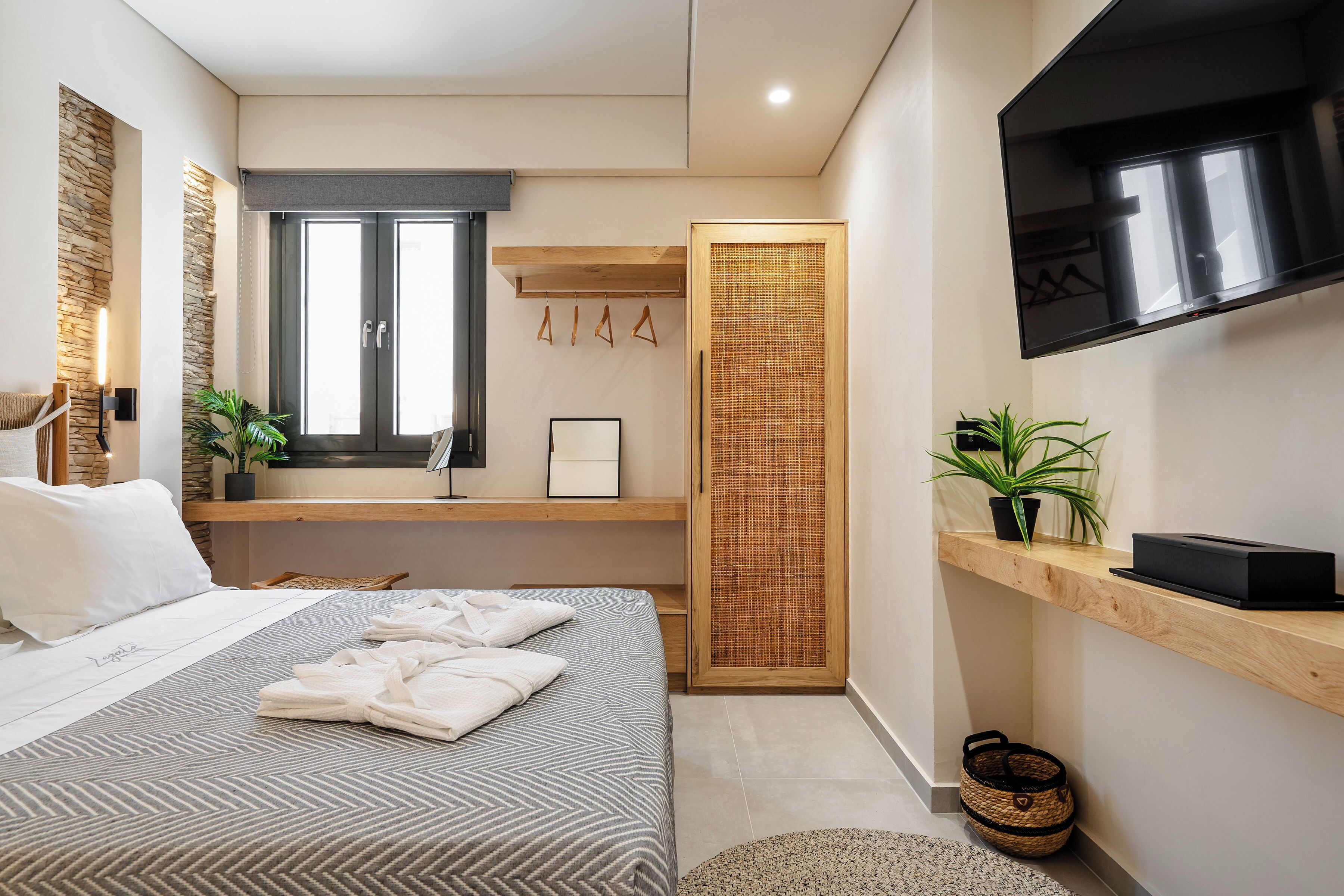 Una habitación de hotel moderna con una cama, televisión, repisa de madera y ventana.