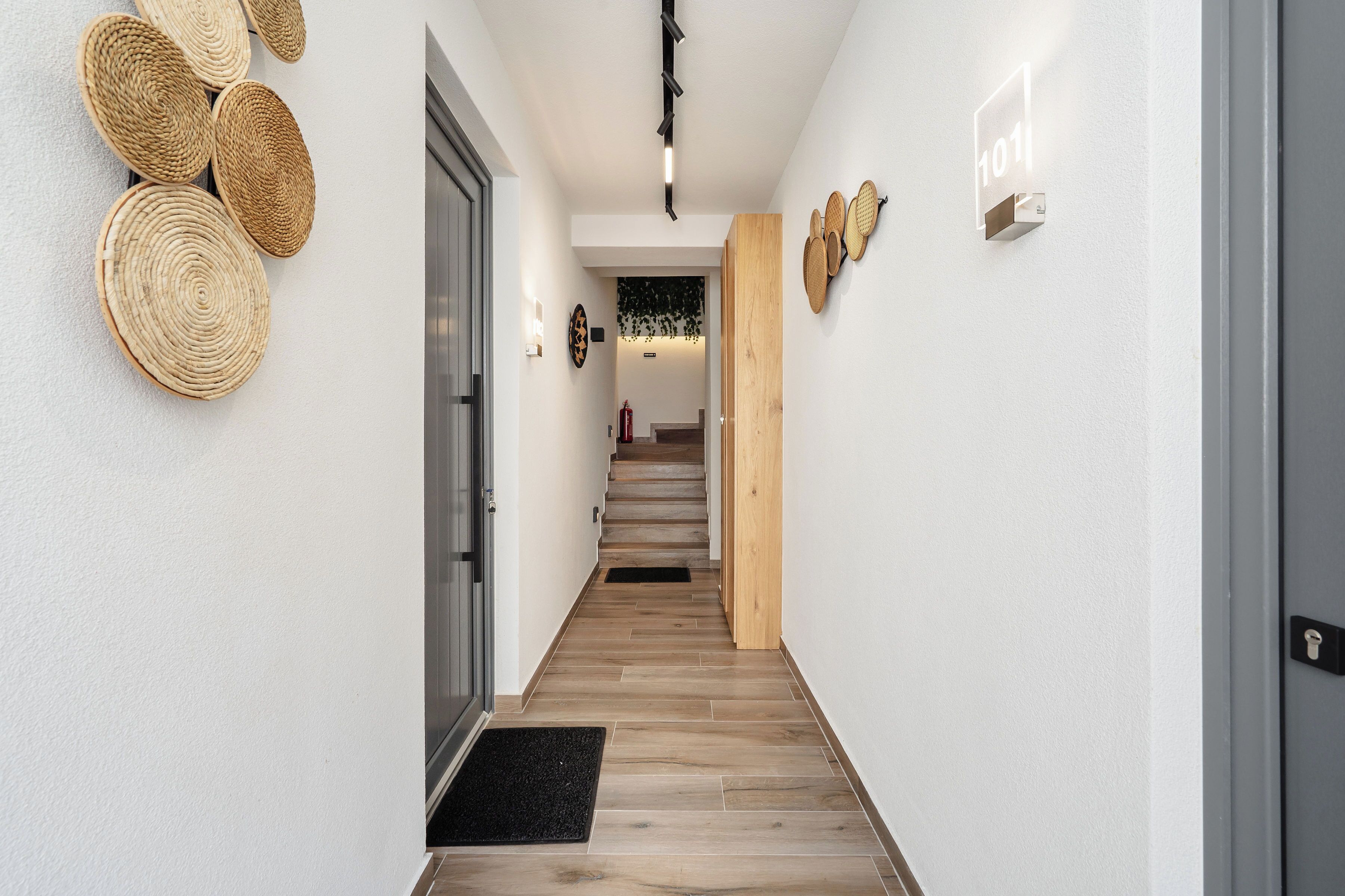 Un pasillo con piso de madera, felpudo negro y adornos tejidos en las paredes.