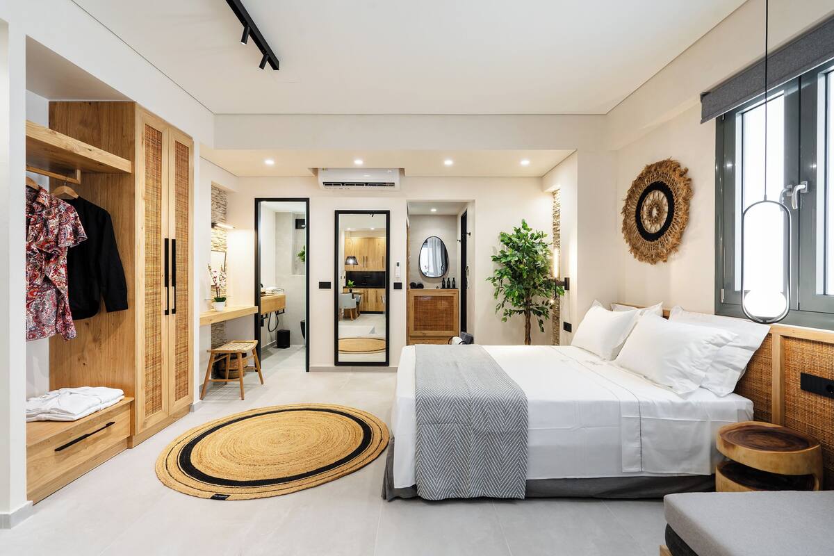 A modern bedroom with a large bed, a wardrobe, a bathroom, and a view of the kitchen.