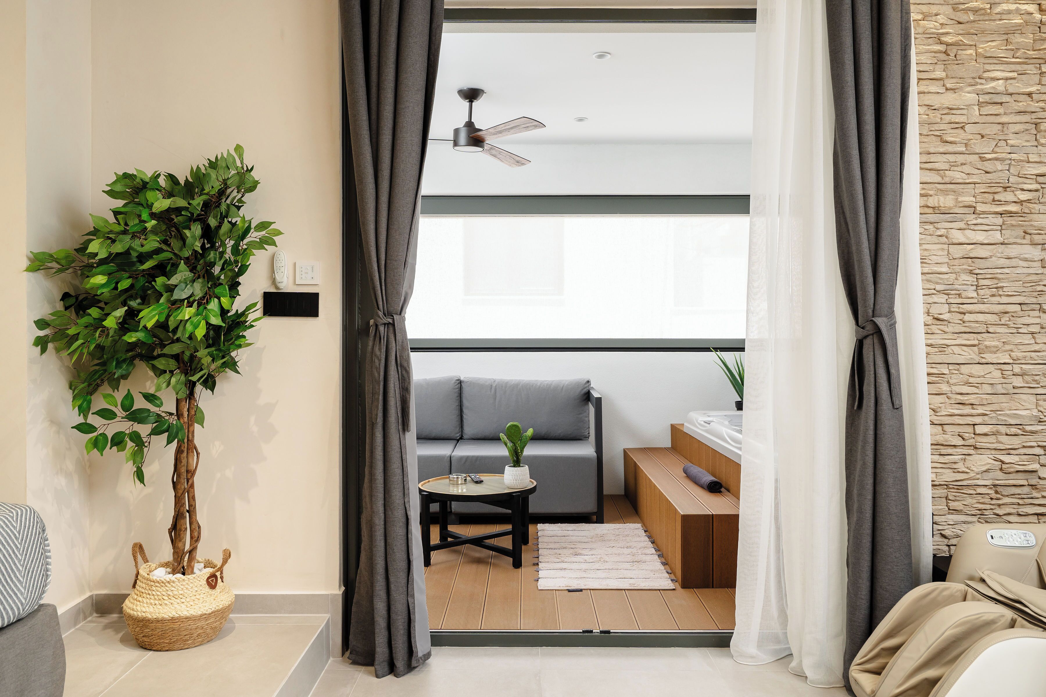 A modern living room with a grey sofa, a small round table, a ceiling fan, and a large plant.