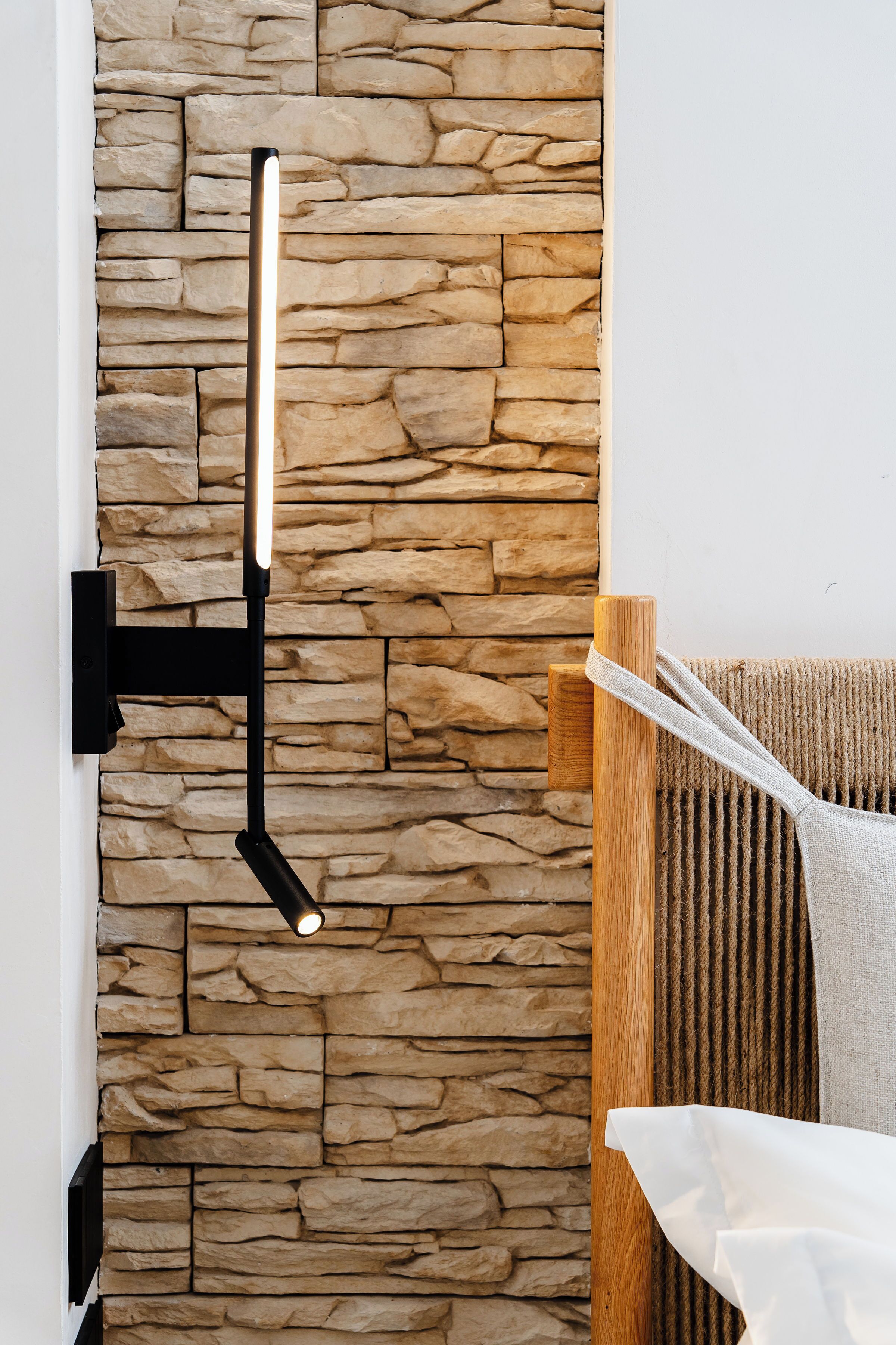 A wall-mounted light fixture against a stone wall, a wooden chair, and a white towel.