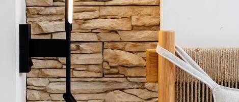 A wall-mounted light fixture against a stone wall, a wooden chair, and a white towel.