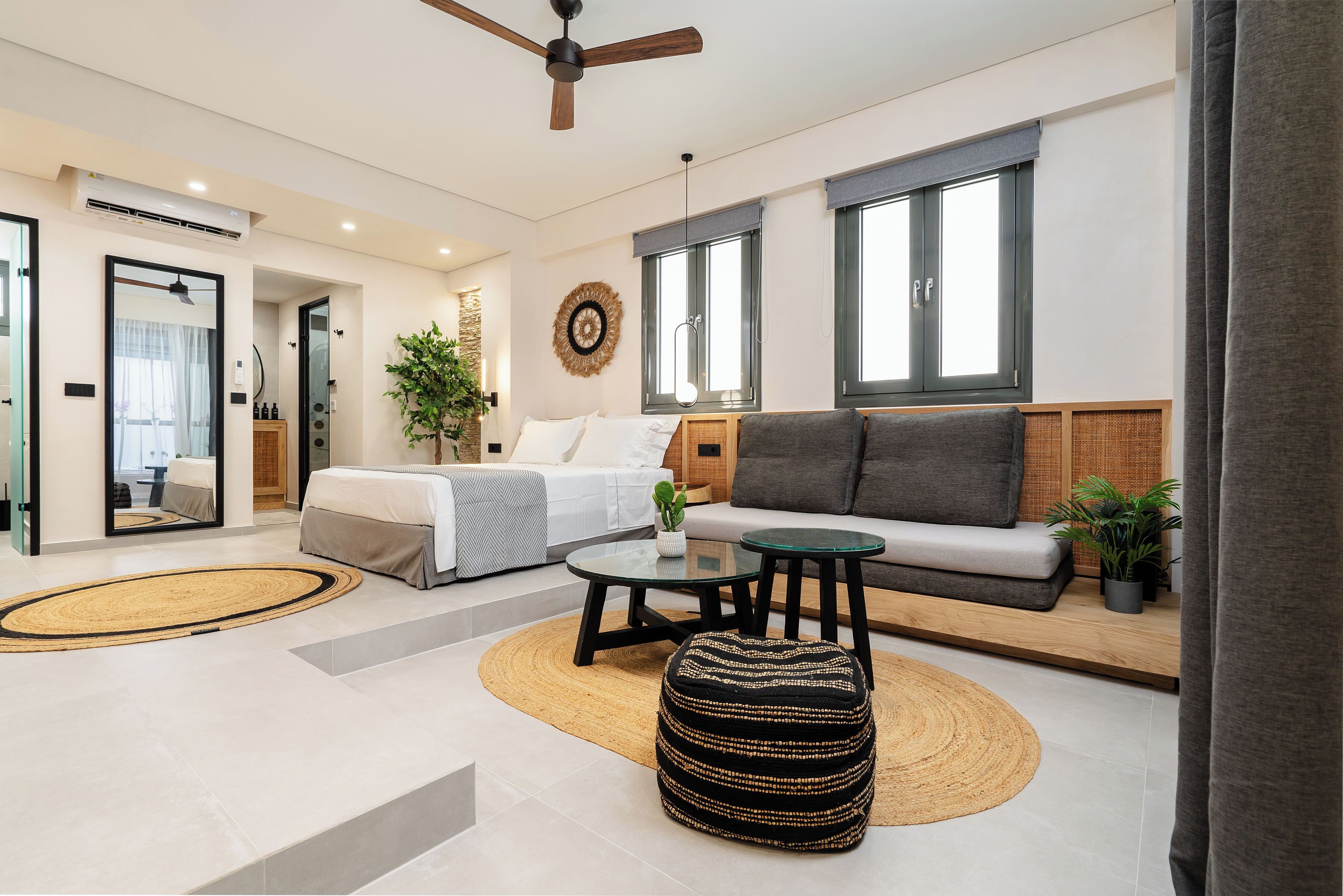 A modern living room with a sofa, ottoman, and coffee table, a bed with a view, and a large window.
