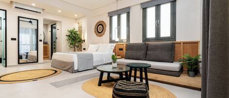 A modern living room with a sofa, ottoman, and coffee table, a bed with a view, and a large window.