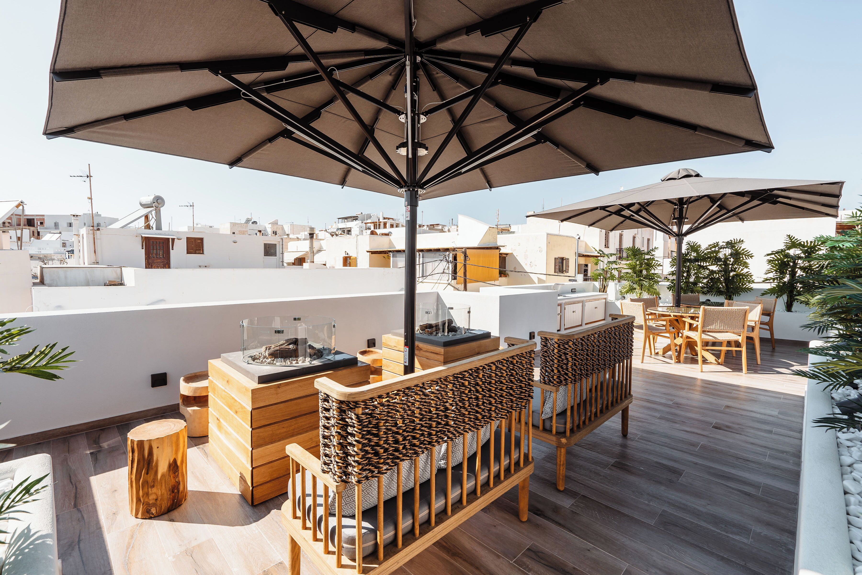 Terraza en la azotea con mobiliario de madera, sombrillas grandes y vistas panorámicas de la ciudad.