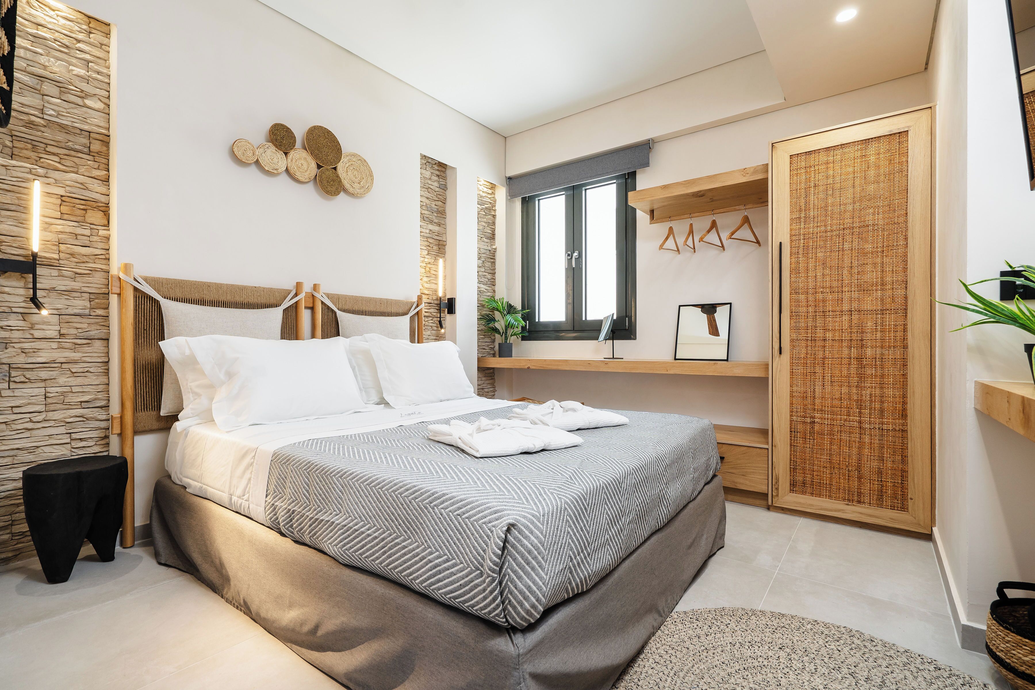 A modern bedroom with a large bed, a stone accent wall, a wooden headboard, and a large window.