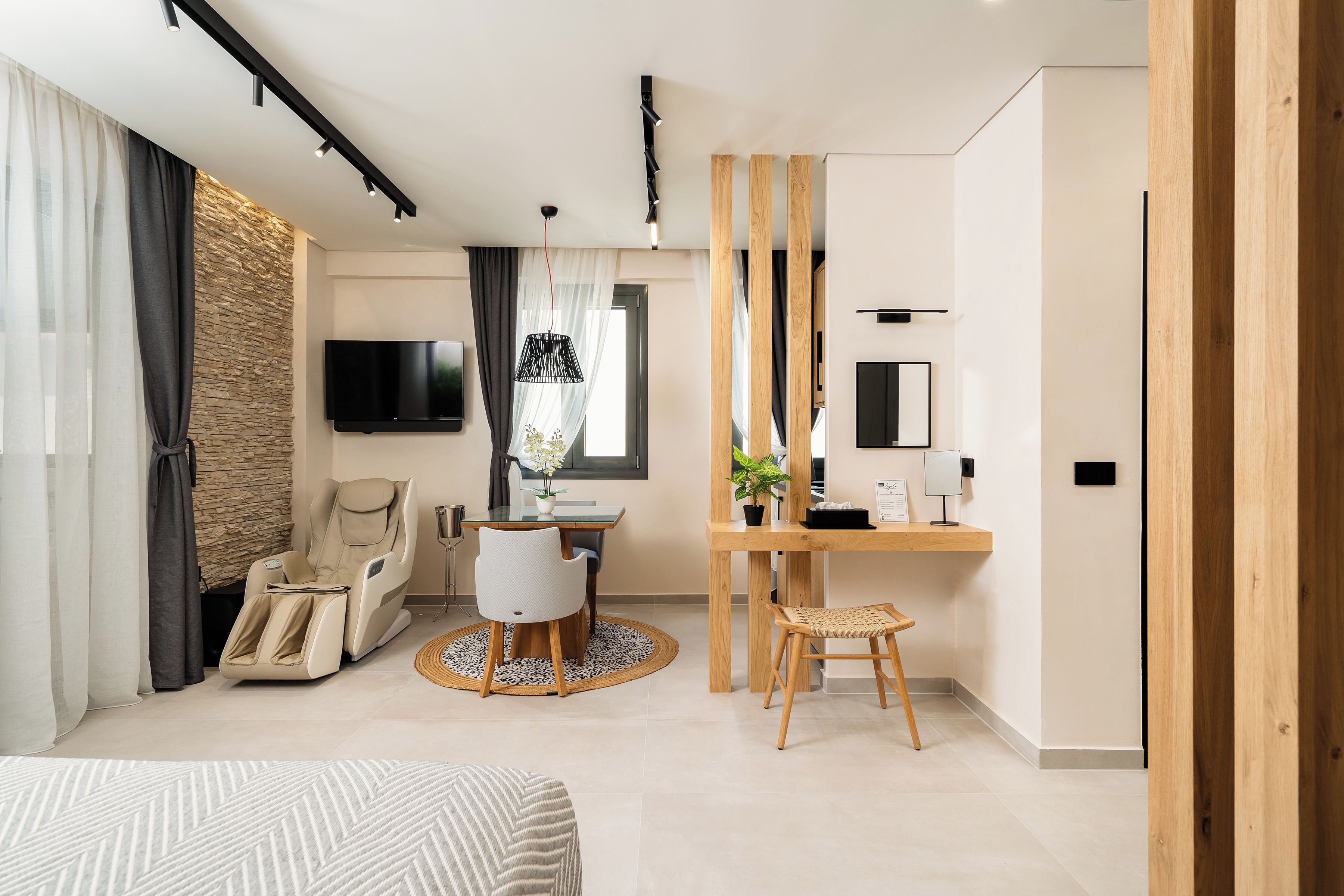 A modern hotel room with a massage chair, a dining area with a round table, a TV mounted on the wall, and a wooden partition.