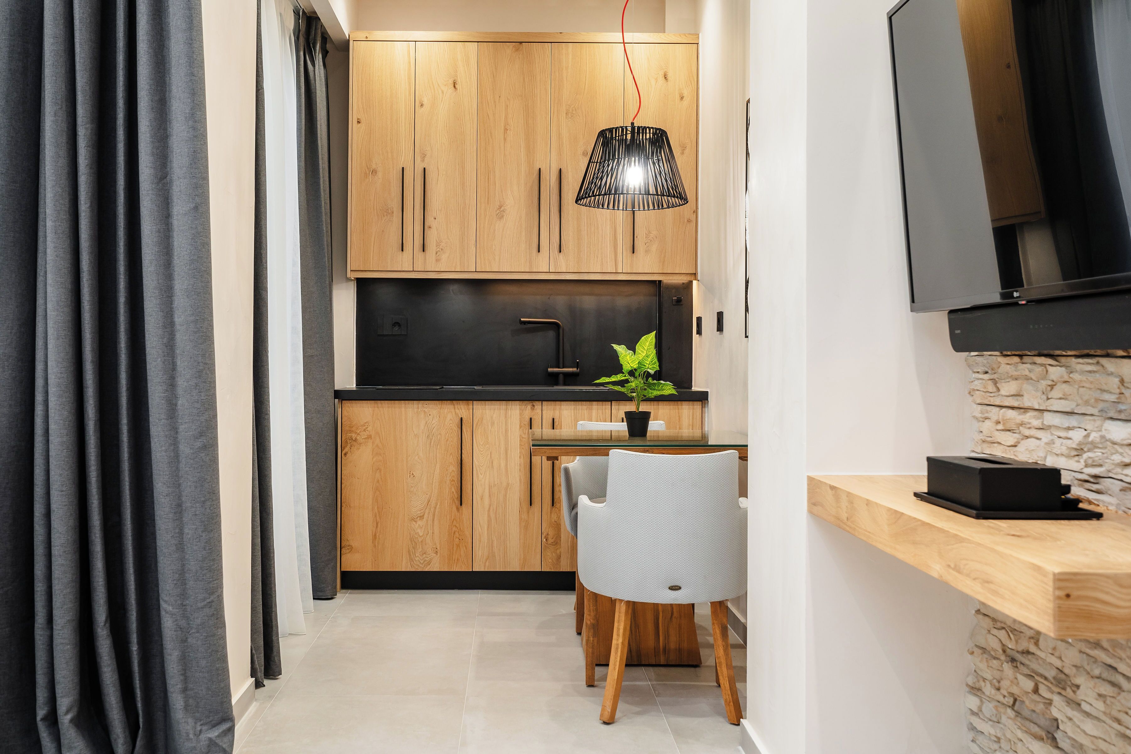 Una cucina compatta con mobili in legno, un piano di lavoro nero, un tavolo da pranzo con sedie, una pianta in vaso e una TV a schermo piatto montata a parete.