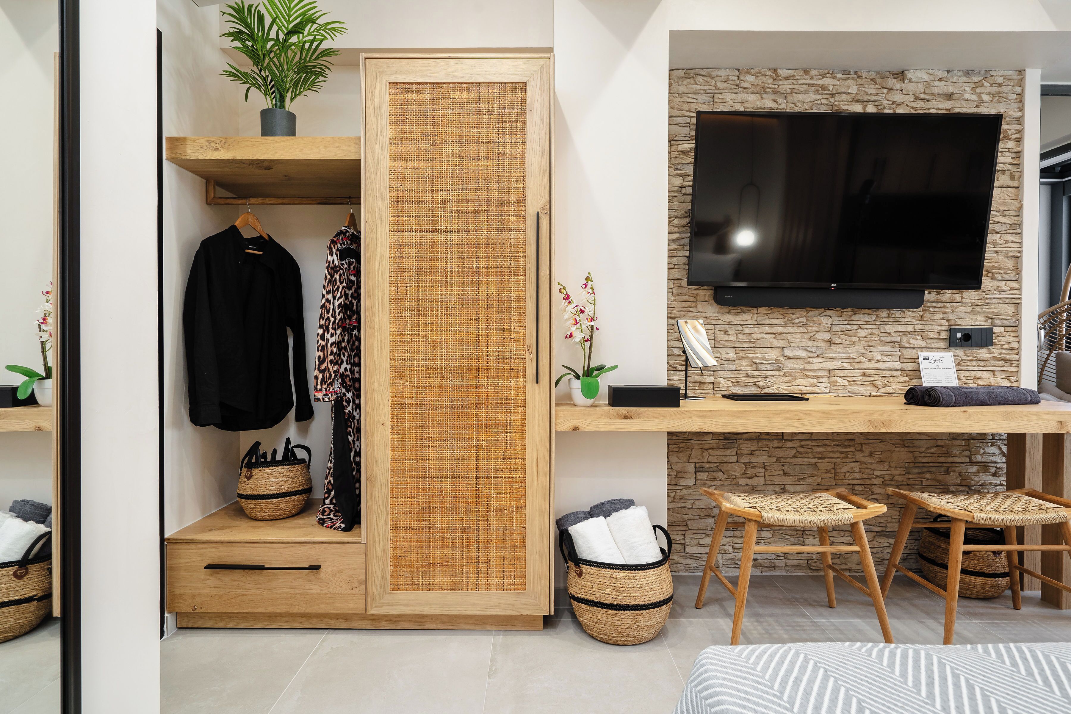 Una habitación moderna con un escritorio de madera, un televisor de pantalla plana, cestas de mimbre y un armario con separador tejido.