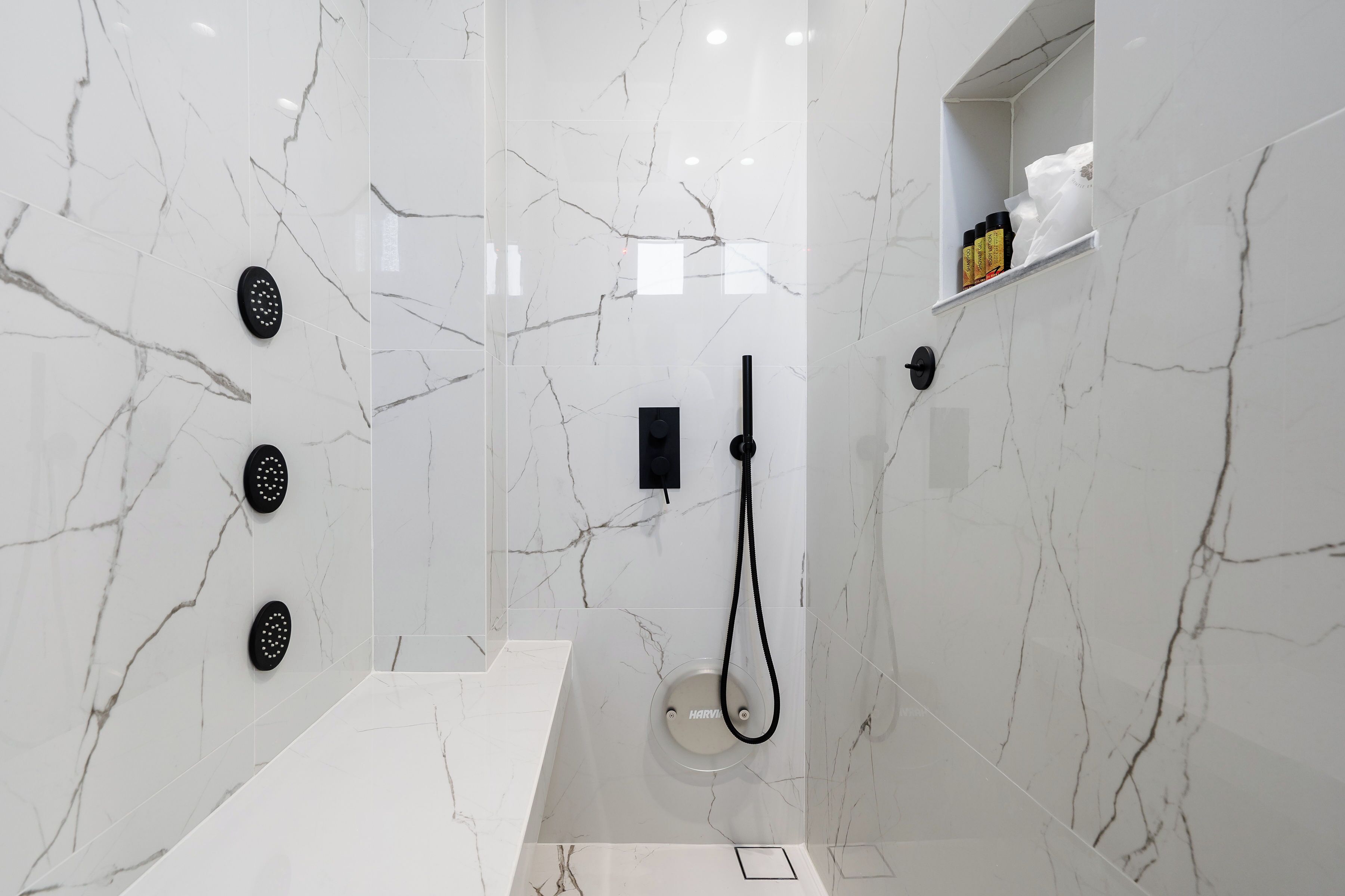 Ein modernes Badezimmer mit weißen Marmorwänden, einer integrierten Dusche und einem Ablagefach für Pflegeprodukte.