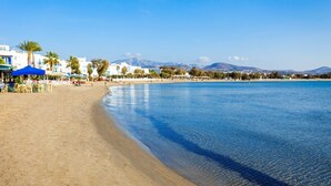 A beach with clear blue water, a sandy shore, and buildings in the background. - Legato Spa Suites (Naxos)