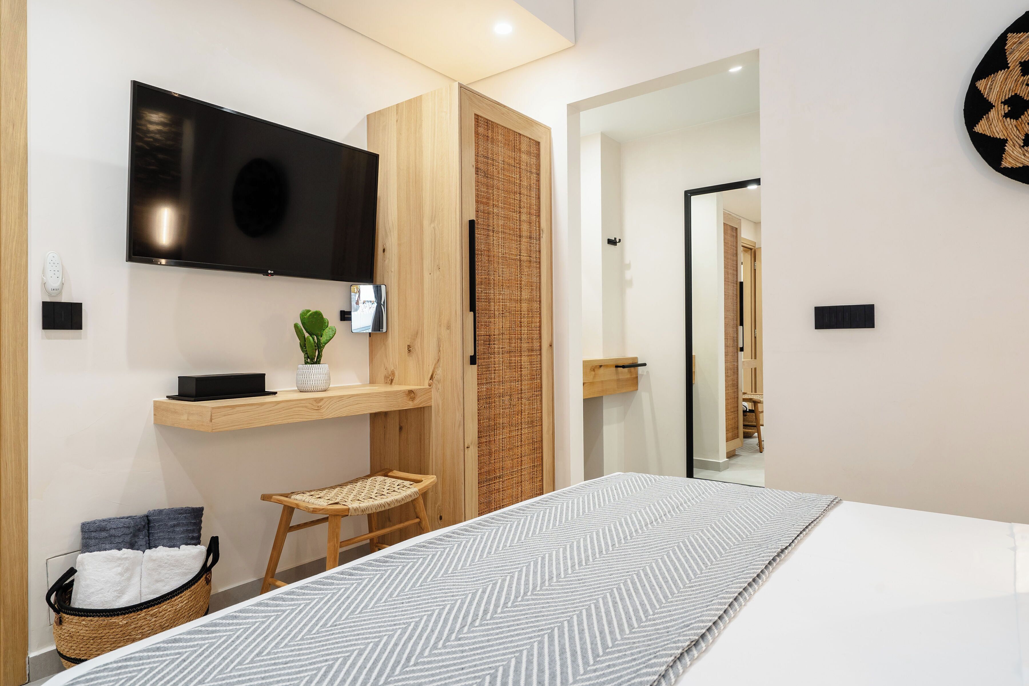 Un dormitorio moderno con una cama grande, un televisor montado, un pequeño rincón de descanso y una cesta con toallas.