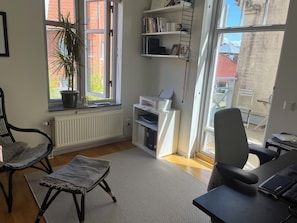 A room with a large window, a radiator, a bookshelf, a desk with a chair, and a potted plant. - Underbart Town House på Ön, Limhamn med Alla Bekvämligheter (Skåne län)