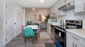 A modern kitchen with white cabinets, stainless steel appliances, and a dining area with teal chairs and a white table. - Adorable 1 bedroom suite - 8mins from West Edmonton Mall (Edmonton)