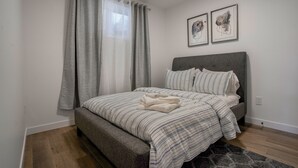 A bedroom with a bed, grey curtains, and two framed pictures on the wall. - Adorable 1 bedroom suite - 8mins from West Edmonton Mall (Edmonton)