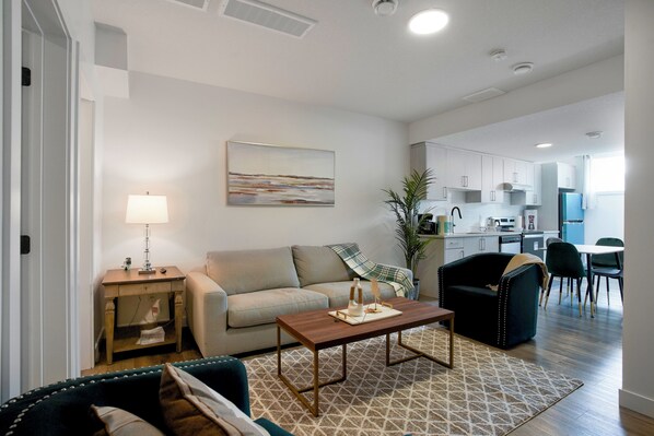 A modern living room with a sofa, coffee table, and a dining area with chairs. - Adorable 1 bedroom suite - 8mins from West Edmonton Mall (Edmonton)