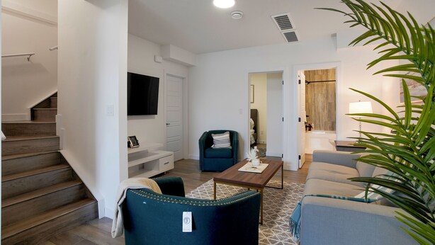 A modern living room with a staircase, a flat-screen TV, a wooden coffee table, and a large plant. - Adorable 1 bedroom suite - 8mins from West Edmonton Mall (Edmonton)