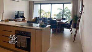 Una cocina moderna con una isla central, comedor con mesa y sillas, y ventanas amplias con vistas a palmeras.