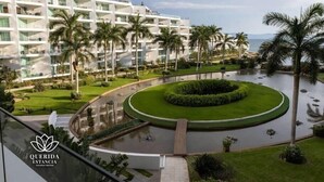 Un hotel moderno con varios pisos, una fuente circular central y palmeras.