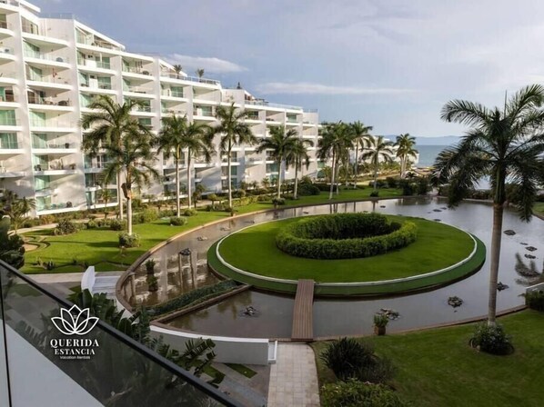 A modern hotel with multiple floors, a central circular water feature, and palm trees.