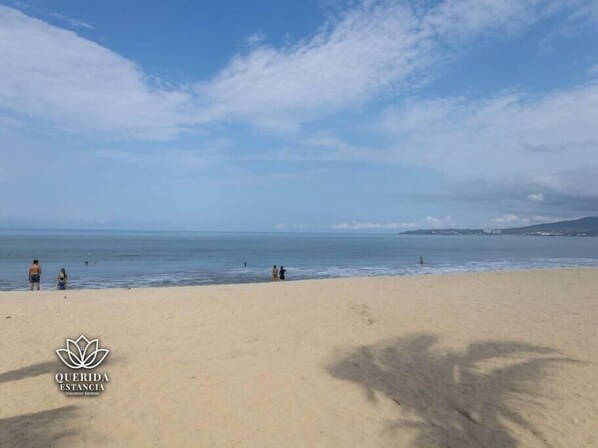 Una playa con el logo de 'QUERIDA ESTANCIA' en la esquina inferior izquierda.