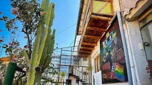 A courtyard with potted cacti, a wooden bench, and a mural on the building wall. - Casa Cusco guest house (Cusco)