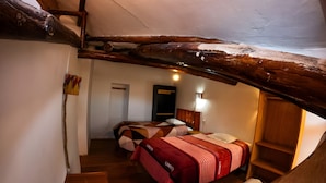 A cozy attic bedroom with a wooden staircase, two beds with patterned bedding, and a small table. - Casa Cusco guest house (Cusco)