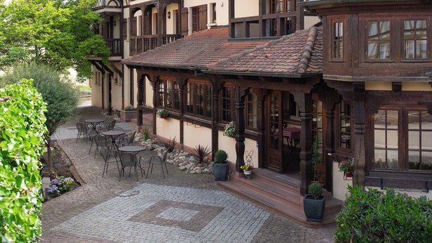 A traditional European courtyard with a cobblestone patio, wooden furniture, and a variety of potted plants. - Hôtel Au Heimbach (Lembach)