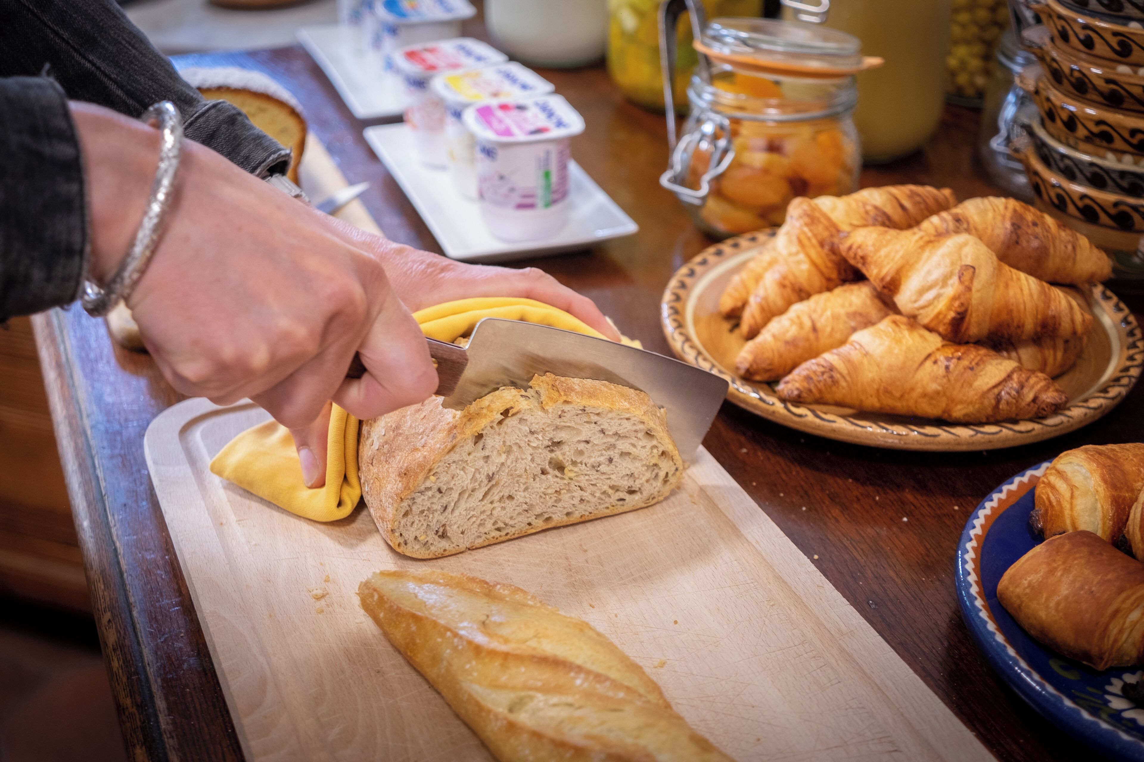 A person slicing a baguette on a wooden cutting board.