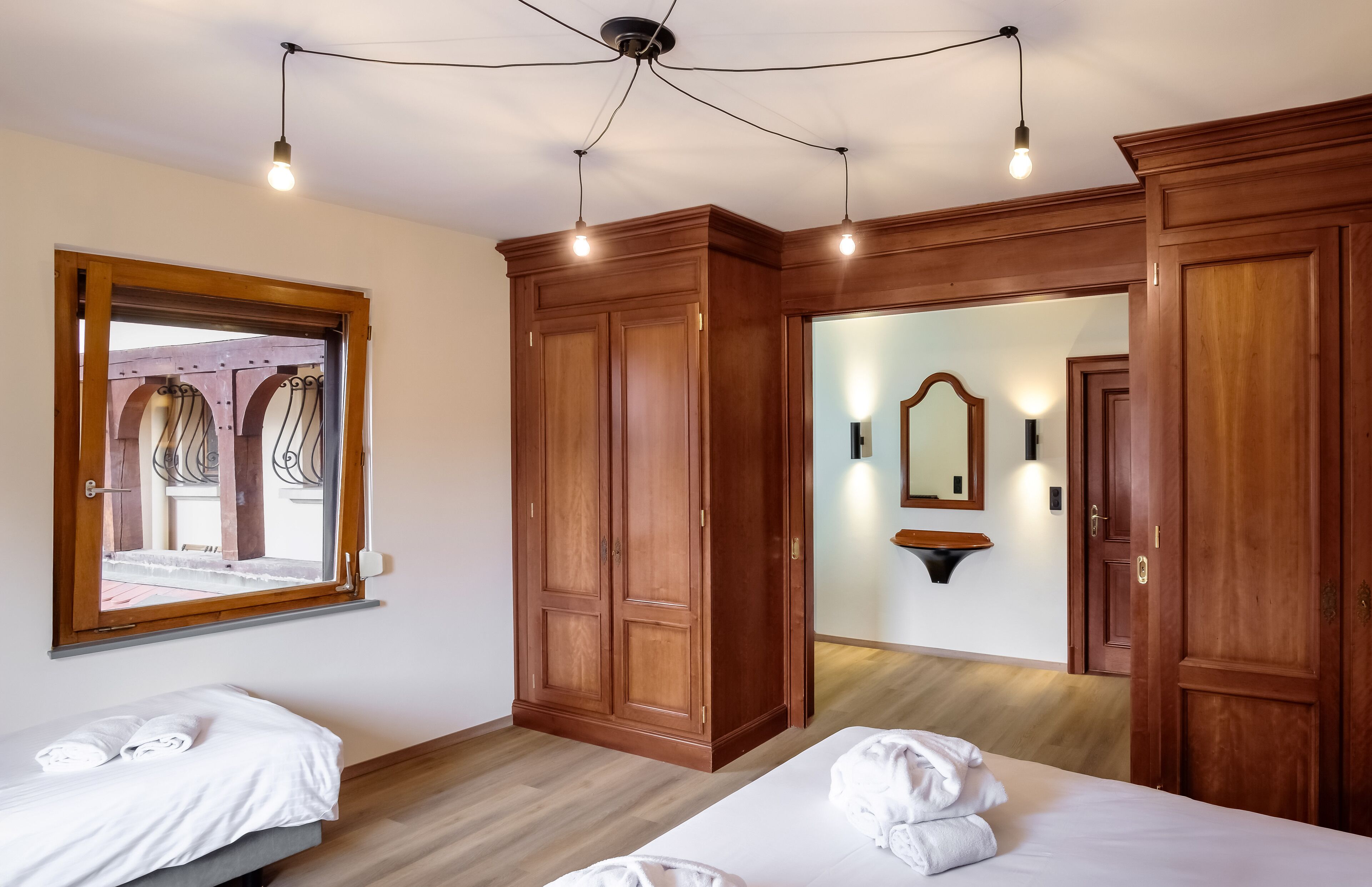 Une chambre d’hôtel avec deux lits, des armoires en bois, un grand miroir et une fenêtre donnant sur un espace extérieur.