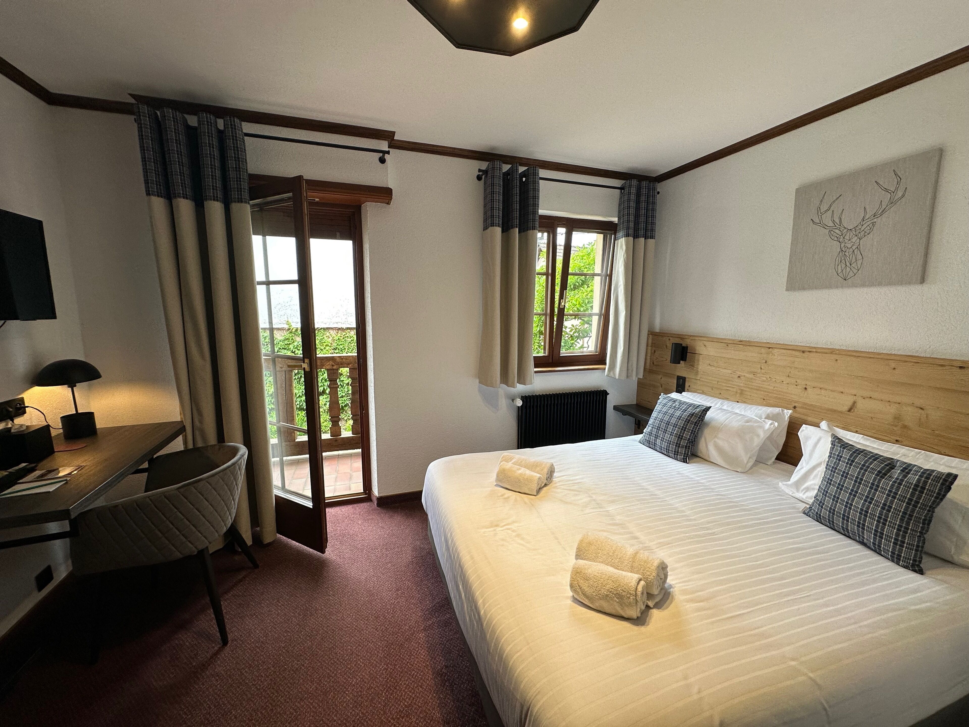 Ein Hotelzimmer mit Bett, Schreibtisch, Stuhl, Fenster mit Vorhängen und Heizkörper.
