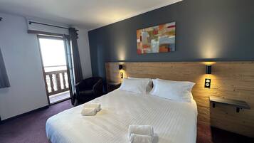 Ein Hotelzimmer mit einem großen Bett, zwei Nachttischen, einem Sessel, einem Bild an der Wand und einer Balkontür.