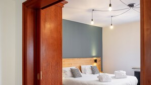A modern hotel room with a wooden door, a bed with white linens, a headboard, and a ceiling light fixture. - Hôtel Au Heimbach (Lembach)