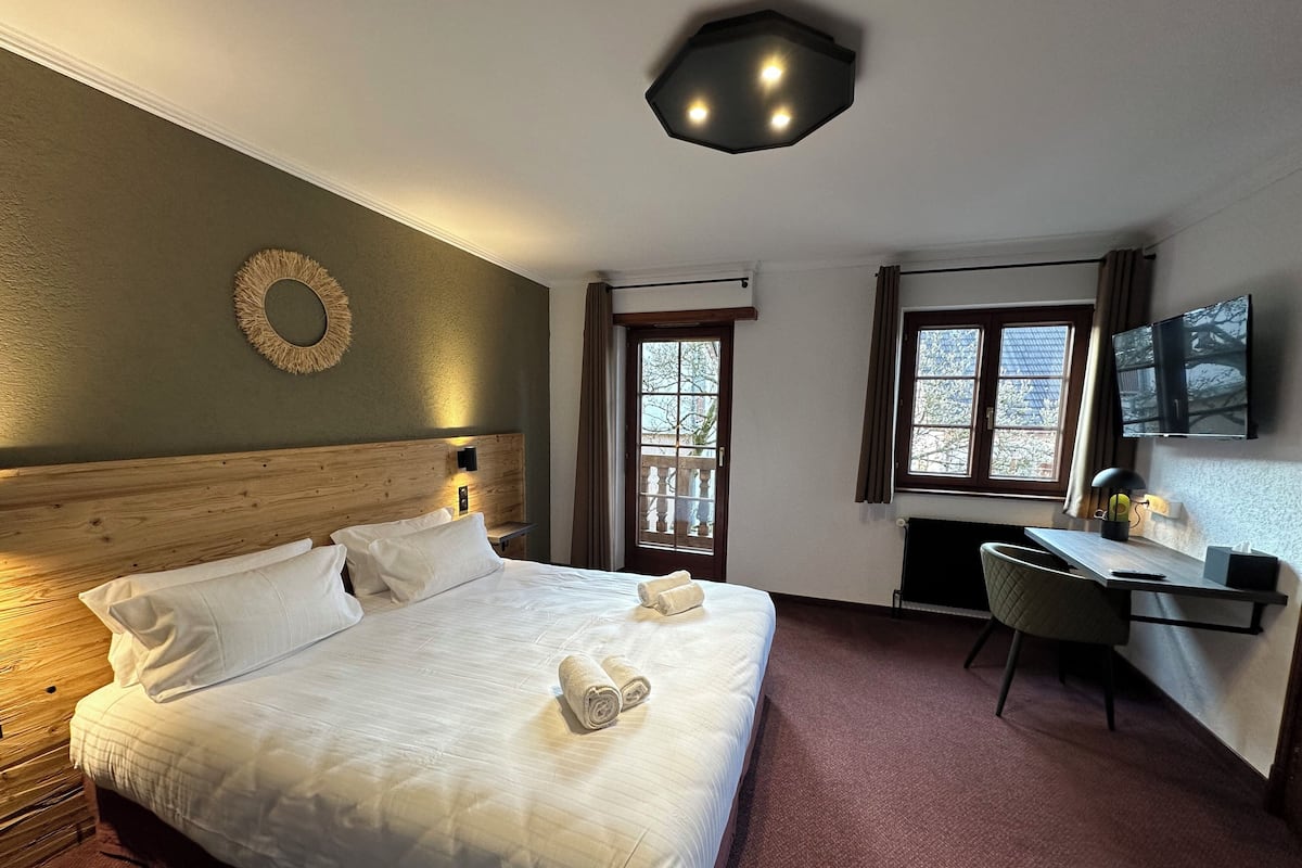 A hotel room with a large bed, a desk, a chair, a TV, and a window with a view.