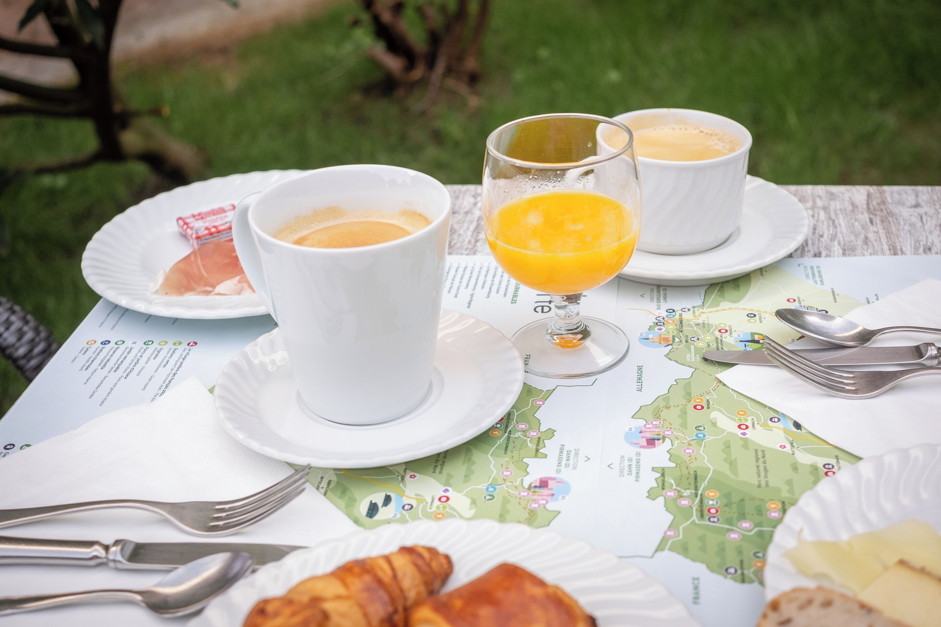 Une table mise pour le petit-déjeuner, avec une carte, des croissants, deux tasses de café et un verre de jus d’orange.