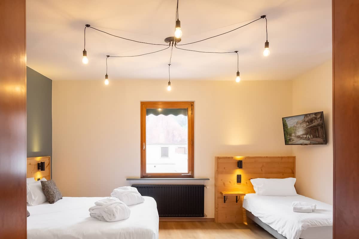 A hotel room with two beds, a wooden headboard, a window with a view, and a painting on the wall.