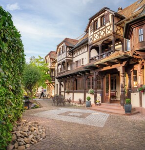 A traditional European courtyard with stone paving, wooden benches, and potted plants. - Hôtel Au Heimbach (Lembach)
