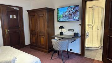 A hotel room with a bed, a desk with a chair, a television, and a shower area.